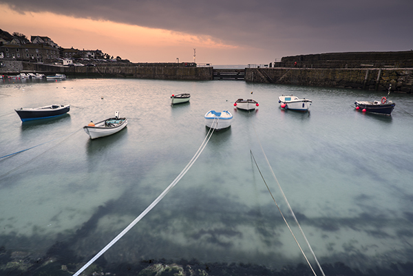 The harbour at St Ives with boats tied to the walls around and floating on clear, clean water. 