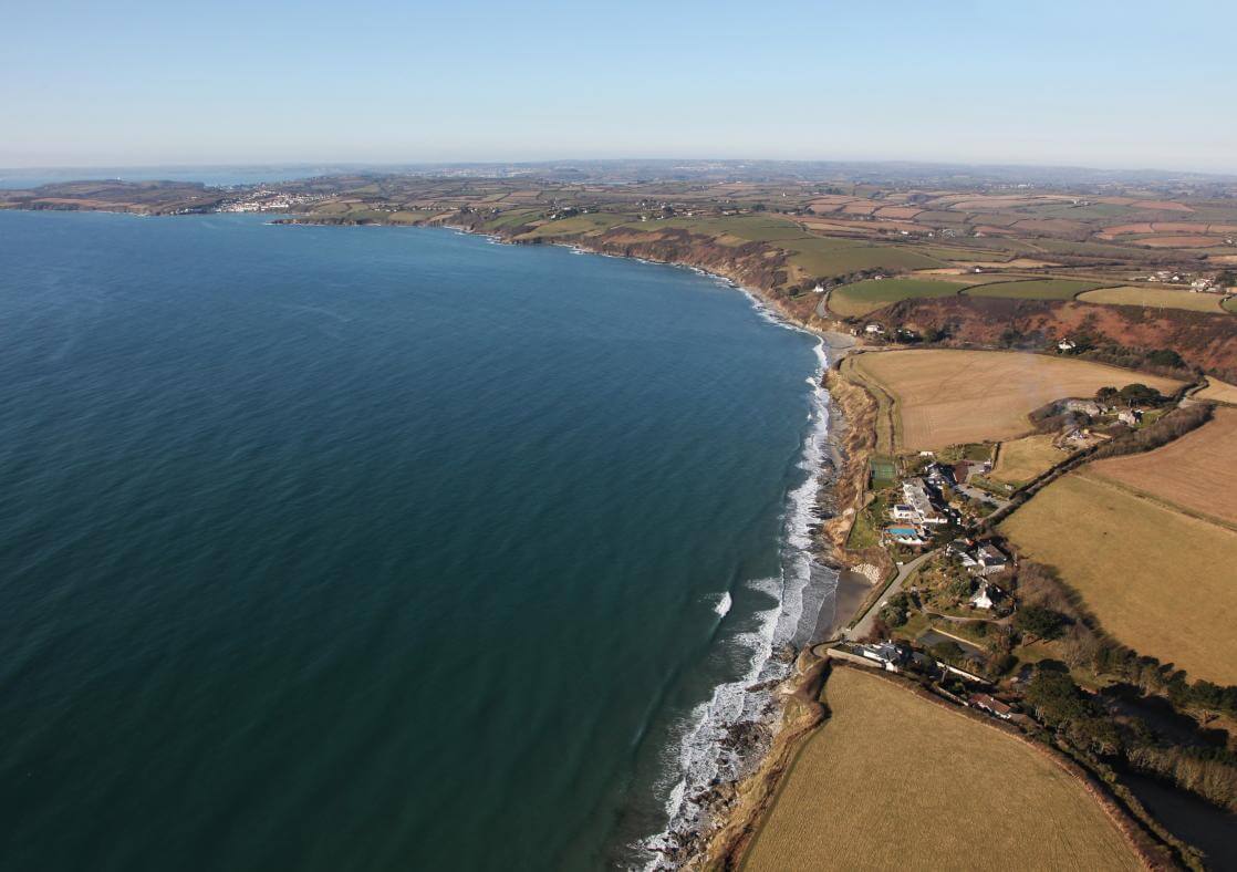 An ariel view of Pendower Beach with the tide in and a perfect blue sky.